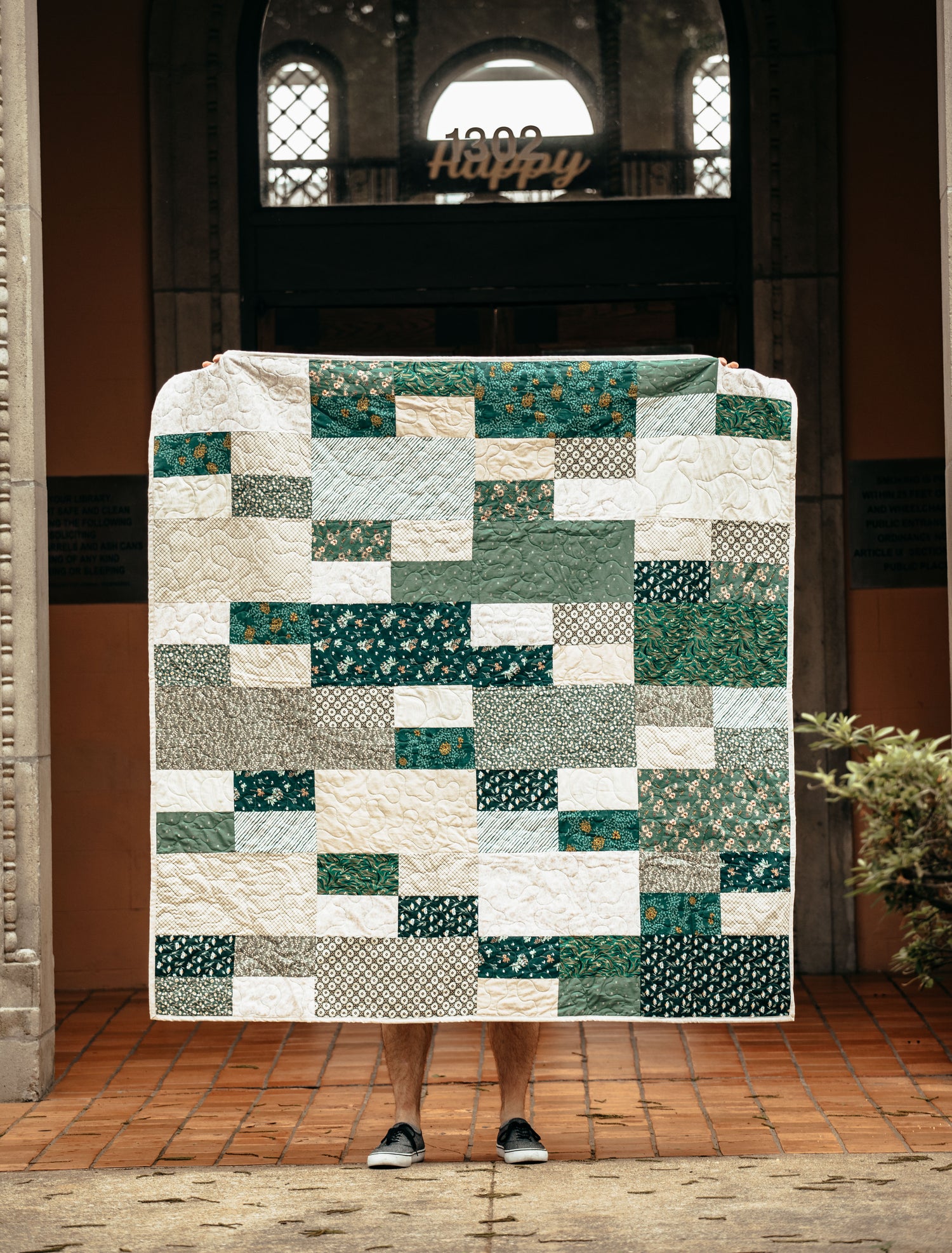 Patchwork quilt with green and white patterns draped over a person in an courtyard setting.
