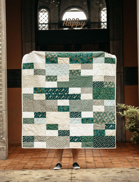 Patchwork quilt with green and white patterns draped over a person in an courtyard setting.